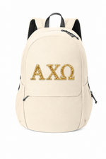 A cream-colored canvas backpack with black straps and zippers, featuring the Greek letters Alpha Chi Omega (ΧΗ) in a textured gold pattern on the front pocket.