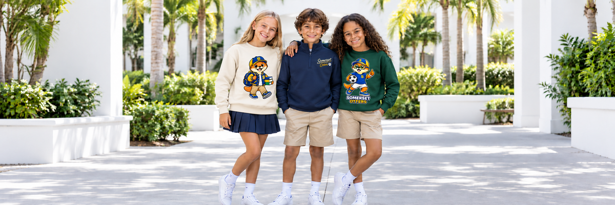 Three children wearing Somerset Avenir Otters apparel in a white school courtyard.